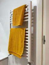 Toallero radiador blanco con dos toallas mostaza colgadas en el cuarto de baño